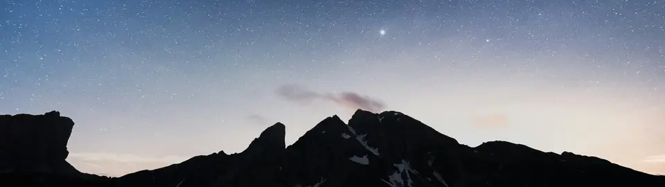 A bright star shining above a snowy mountain range at twilight.