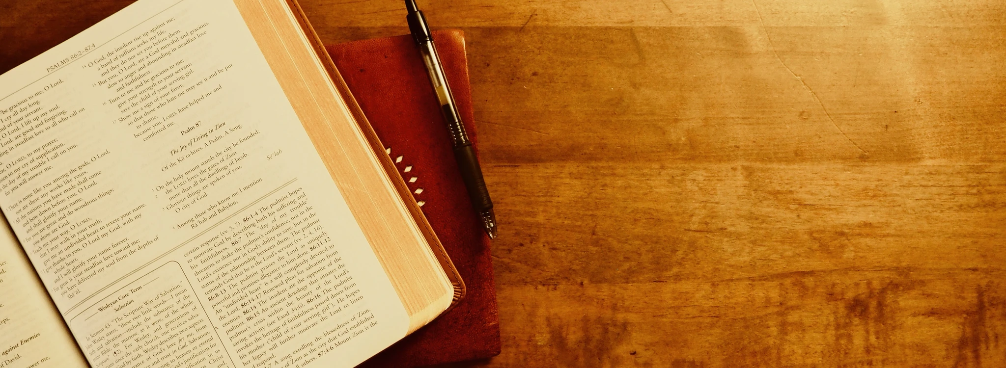 An open Bible and a new notebook sit on a wooden table.