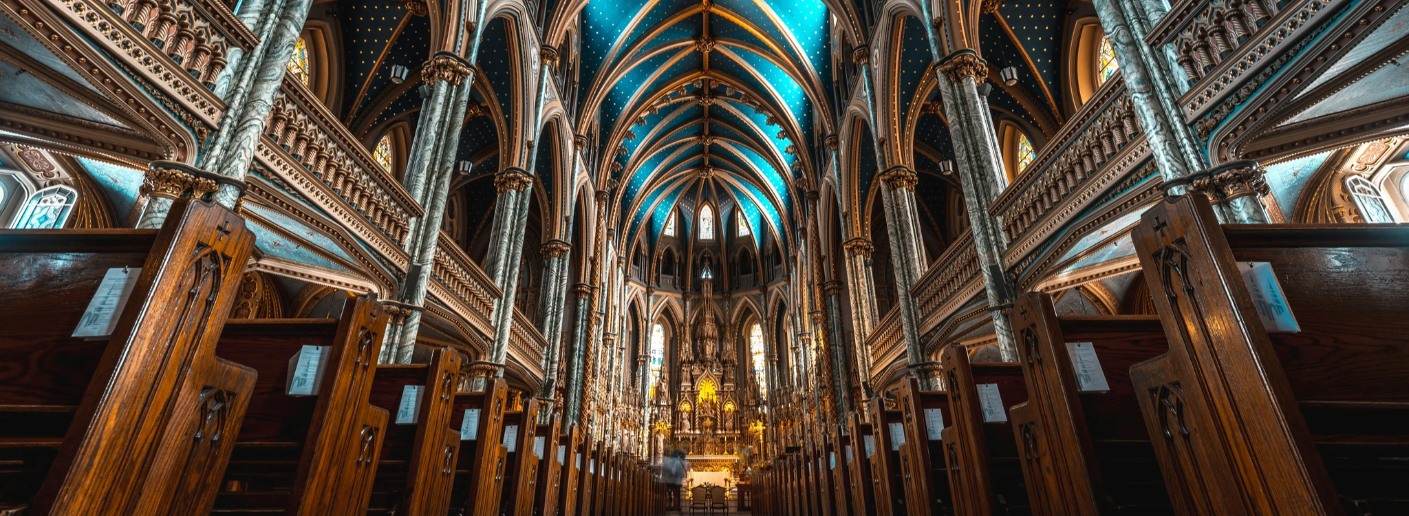 The inside of a cathedral looking past rows of pews to the altar.