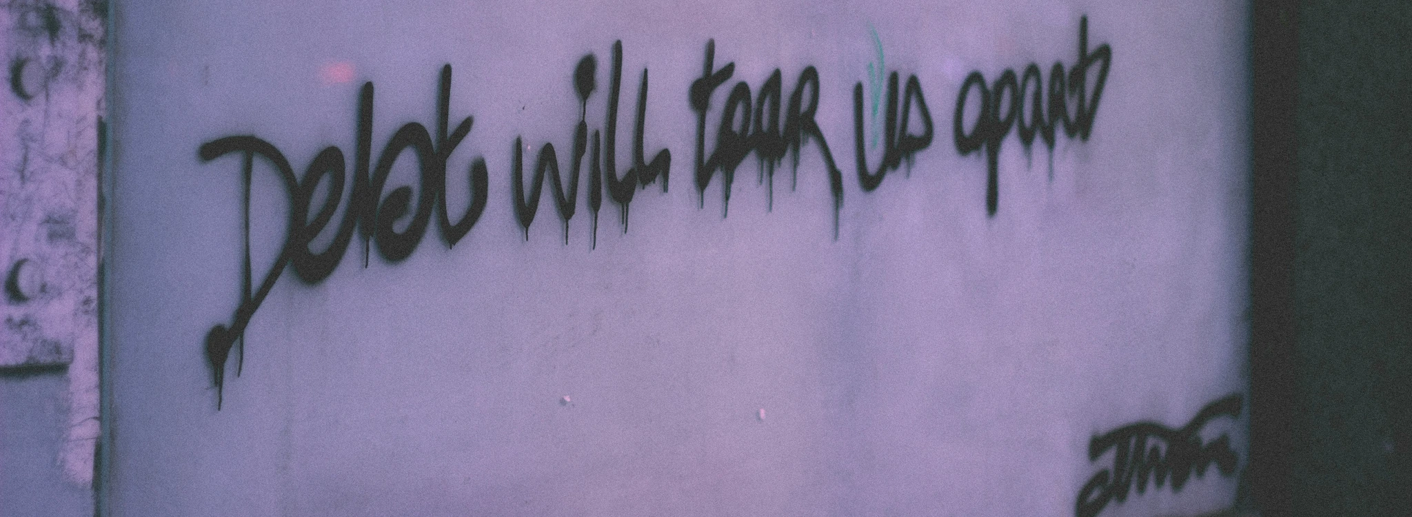 Graffiti on a wall saying ‘debt will tear us apart’